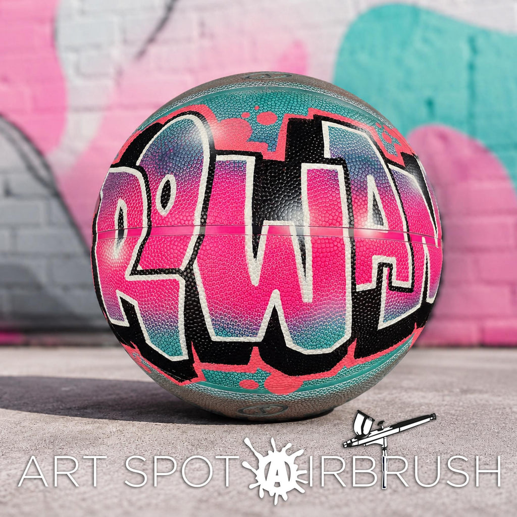 A colorful basketball with the word "ROWAN" painted on it, sitting on a surface against a graffiti-covered wall.