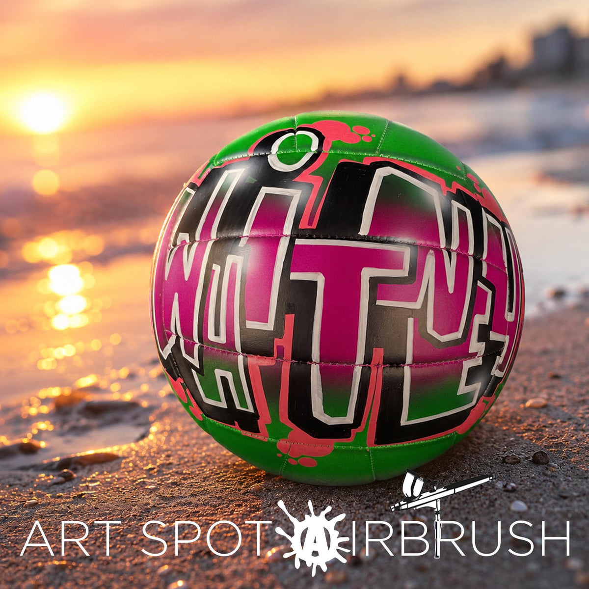 A colorful, graffiti-style custom volleyball personalized with the word "WHITNEY" painted on it, resting on a beach at sunset.