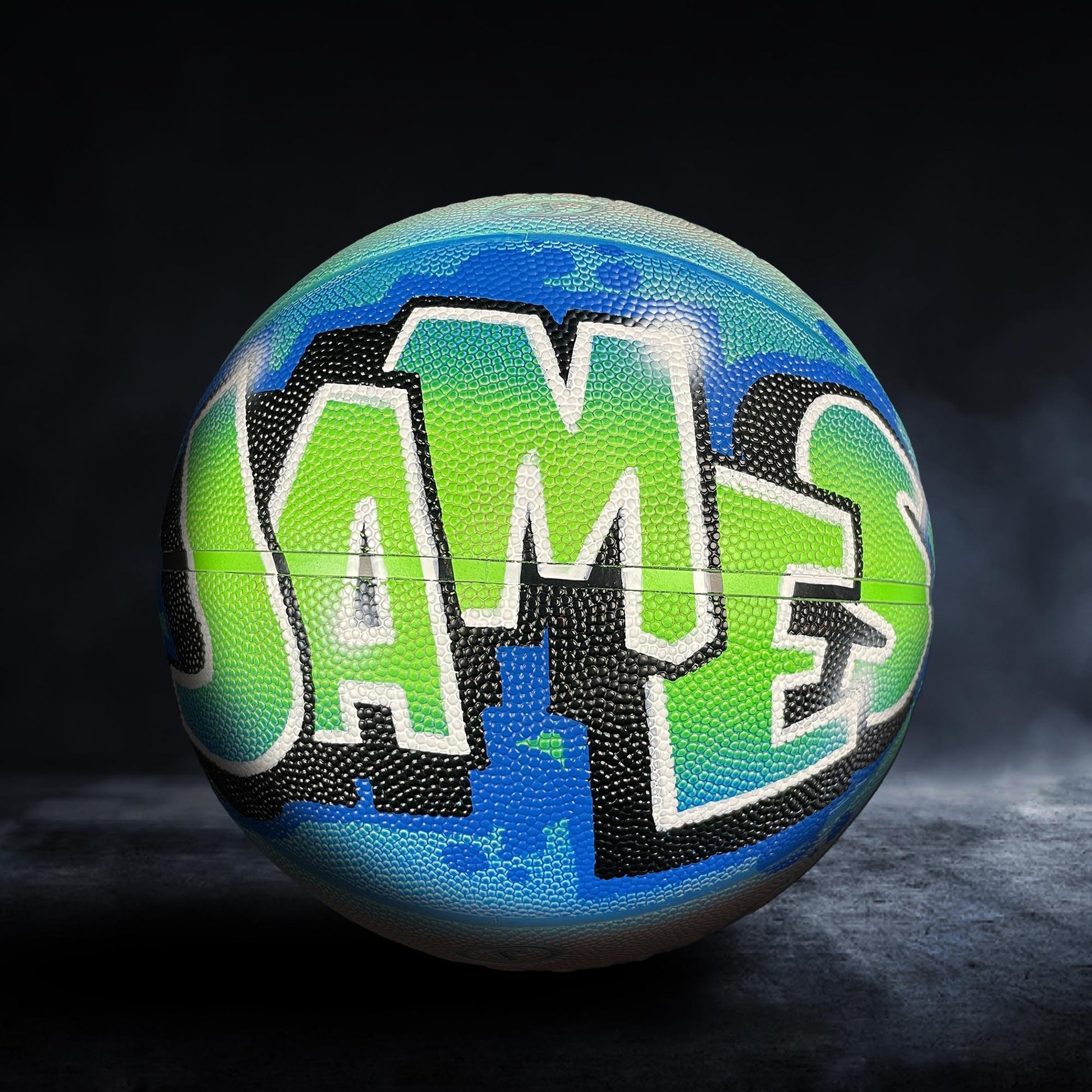 A basketball with the word "JAMES" painted on it in a colorful, graffiti-style design.
