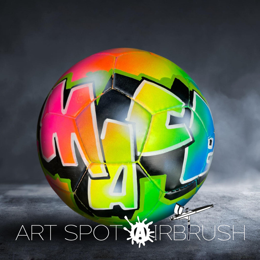 A colorful soccer ball with graffiti-style lettering on it, placed on a dark surface.