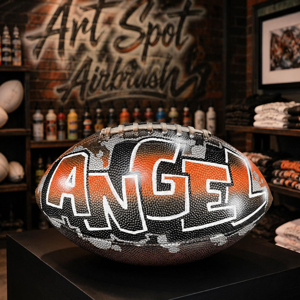 a personalized custom football with the word "ANGEL" painted on it, displayed in a store with various sports equipment and memorabilia visible in the background.