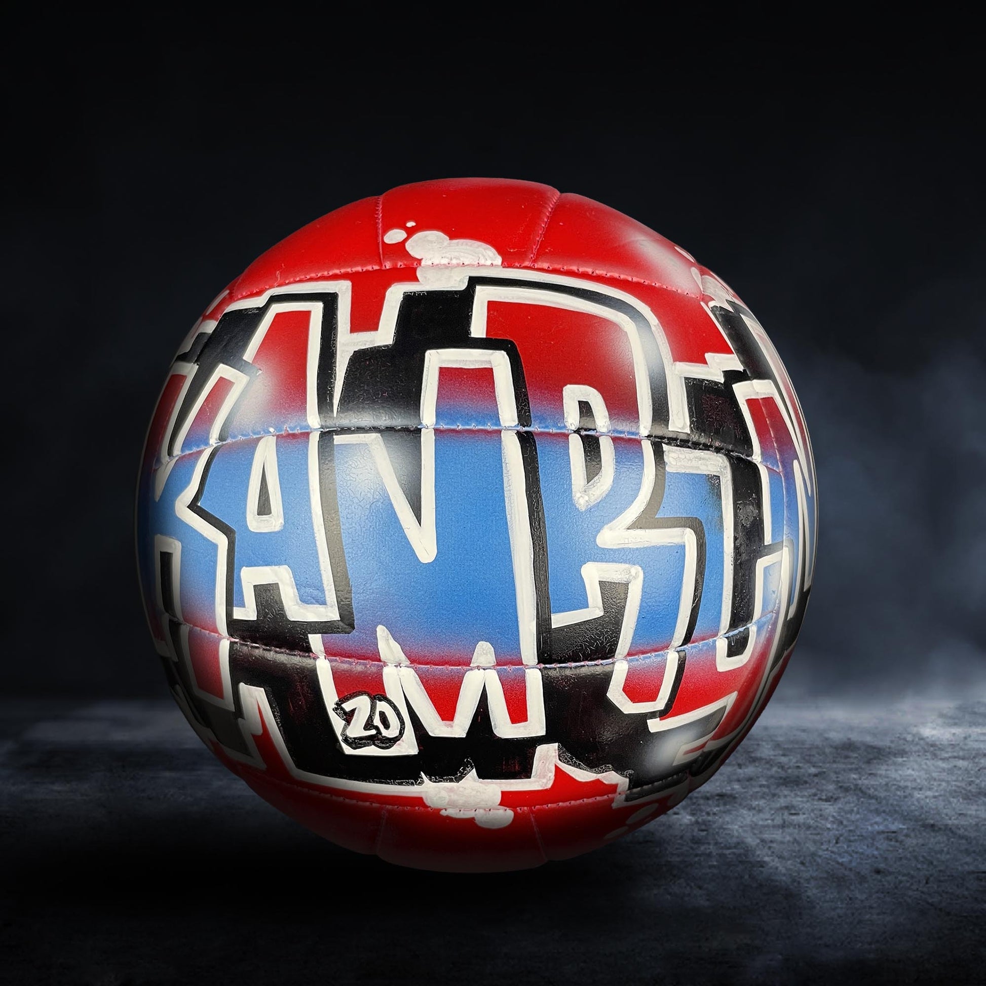 A red and blue soccer ball with graffiti text on it, standing on a dark surface.