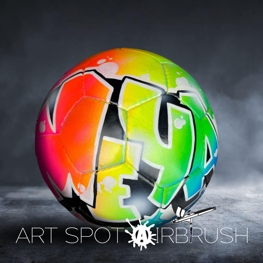 A colorful soccer ball with graffiti-style lettering on it, placed on a dark surface.