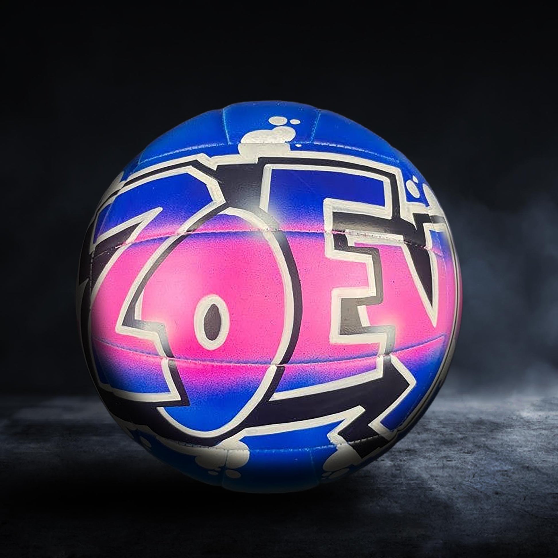 A colorful volleyball with the word "ZOEN" painted on it, set against a dark background.