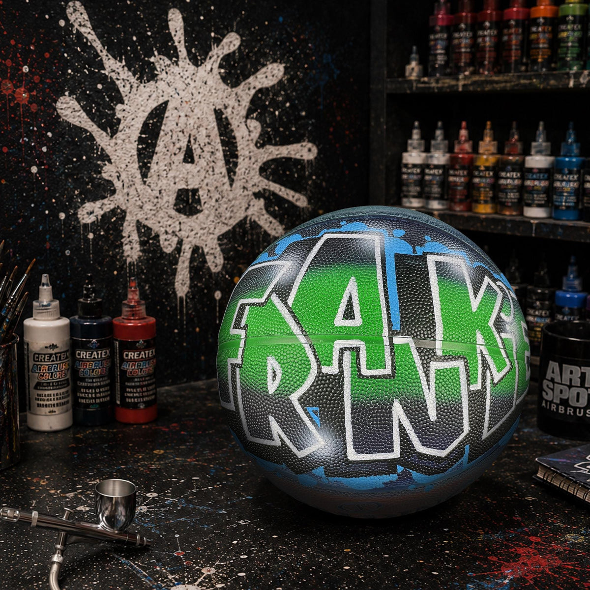 a basketball with the name "FRANK" painted on it, surrounded by various art supplies and spray paint cans on a black surface.