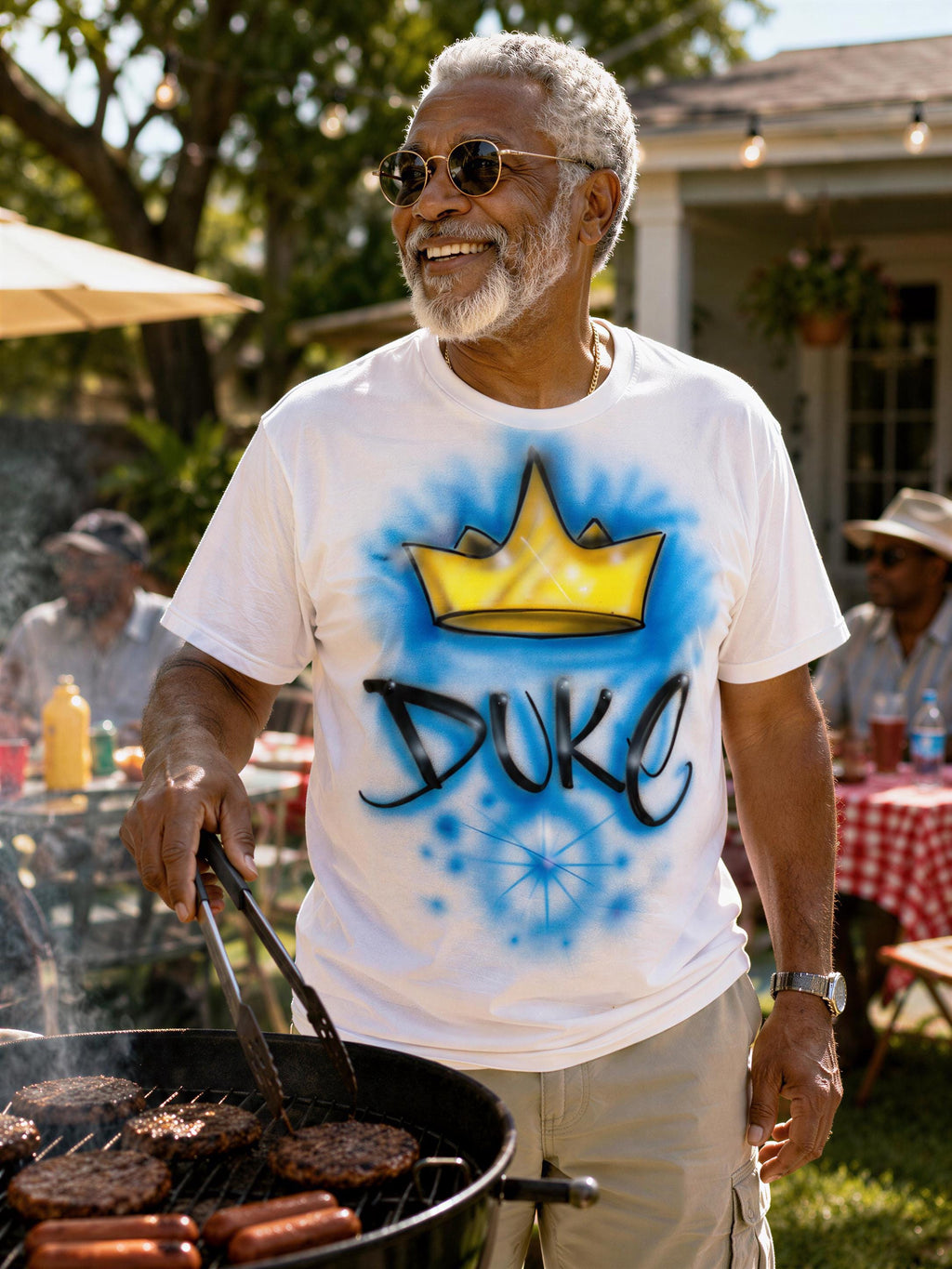 A man wearing sunglasses and a white t-shirt with a crown design is grilling food outdoors.