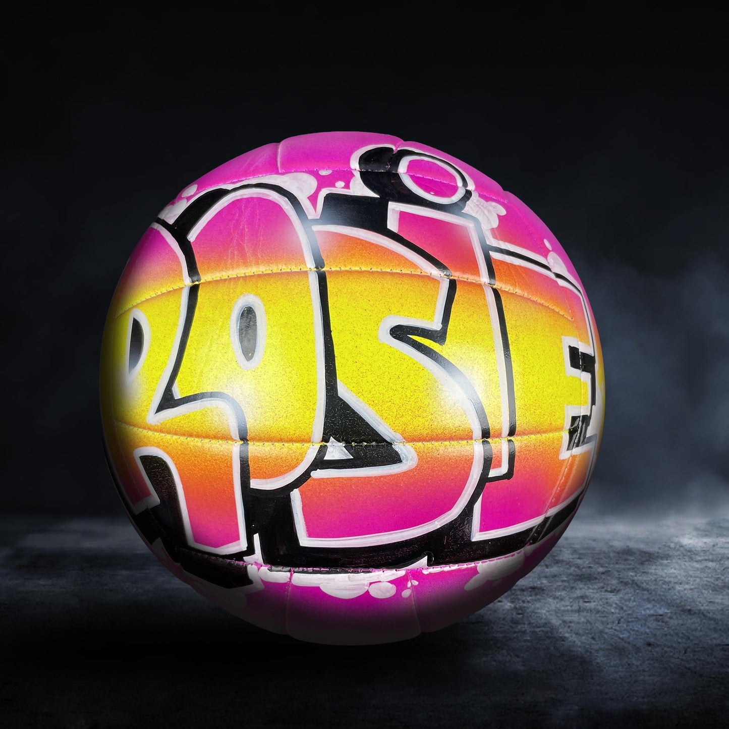 A colorful volleyball with graffiti-style lettering on it, set against a dark background.