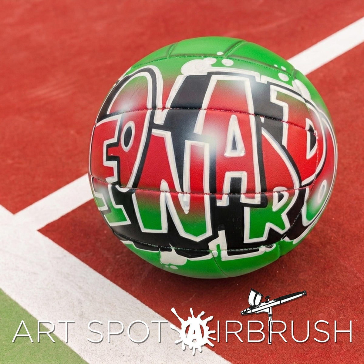 A green and red custom volleyball personalized with graffiti text on it, placed on a red surface.