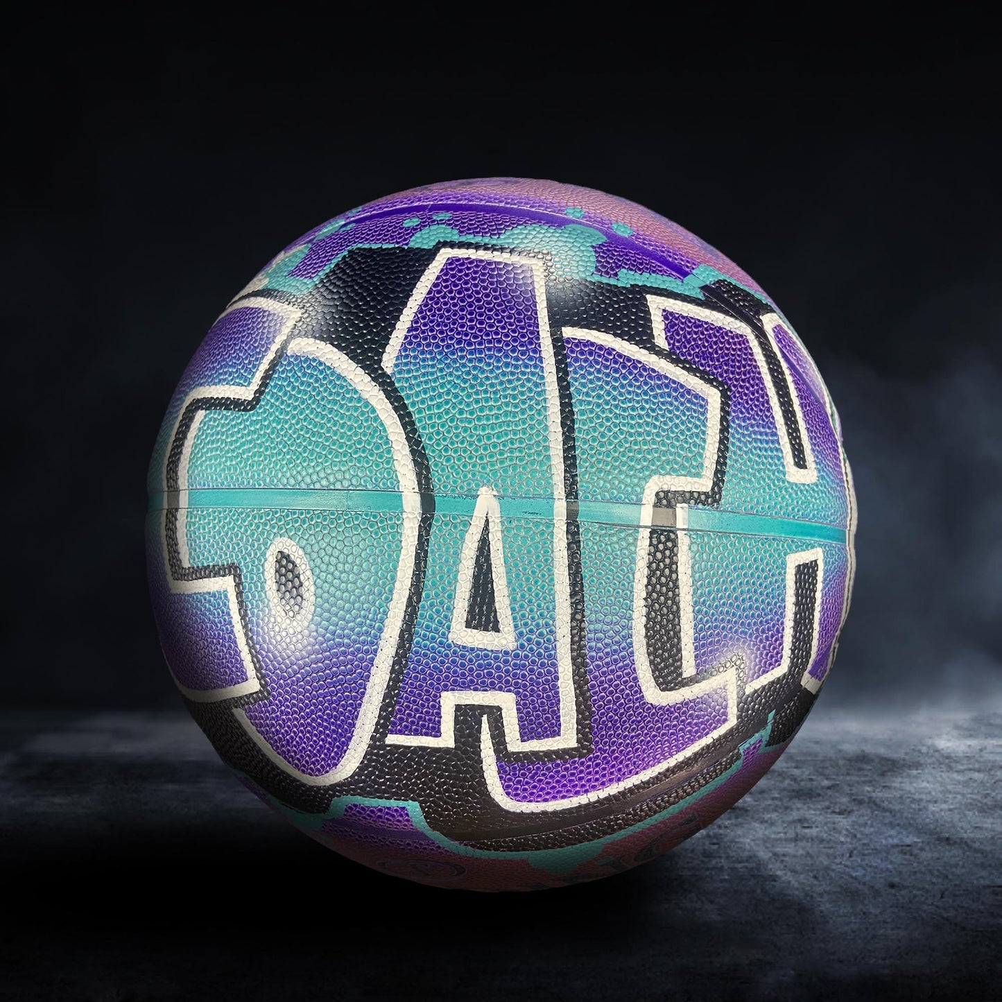 A colorful basketball with the word "COACH" painted on it, set against a dark background.