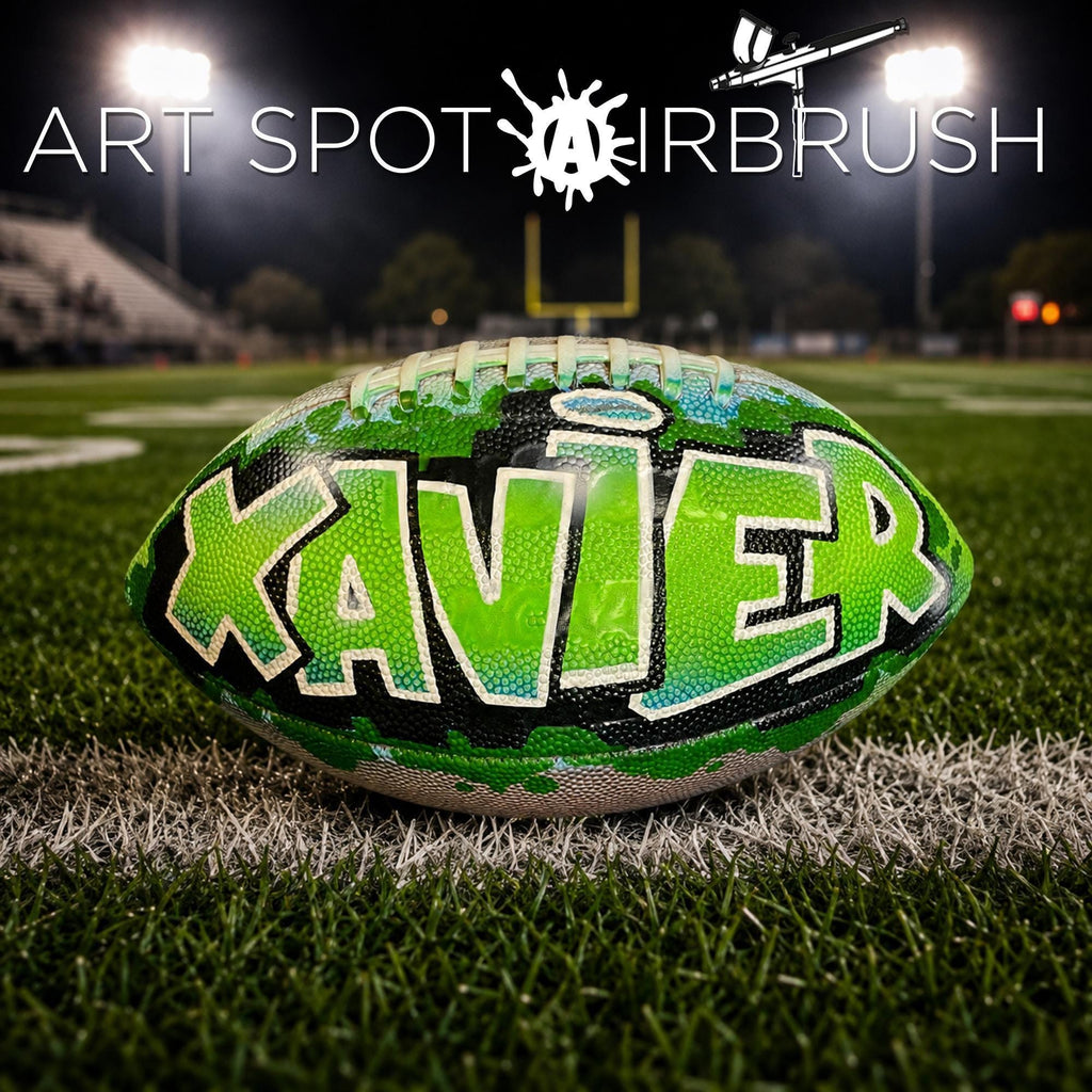 A personalized football with the name "XAVIER" painted on it, placed on a grassy field at night.