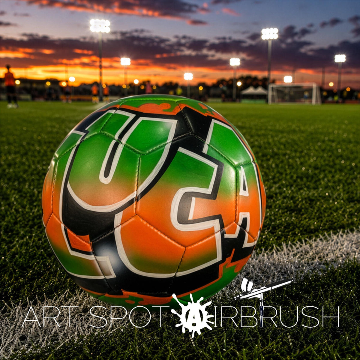 A soccer ball with the letters "UCA" on it, resting on a grassy field at sunset.