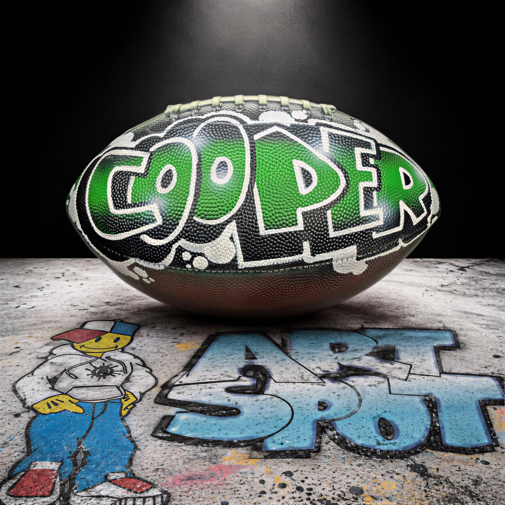 A football with the name "COOPER" painted on it, sitting on a surface with graffiti art below it.