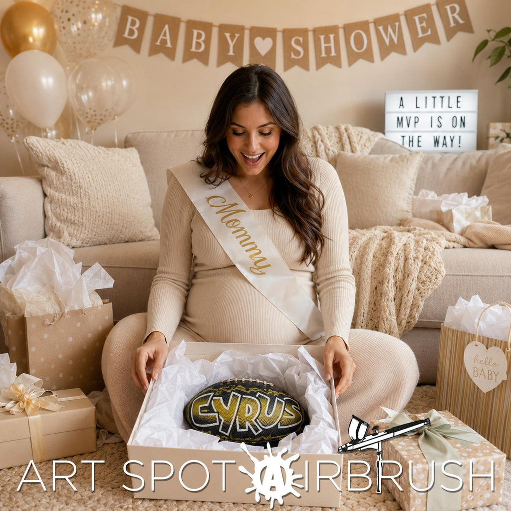 A pregnant woman is sitting on the floor surrounded by gifts, including a large box with apersonalized custom football with the name "CYRUS" and a sign that says "ART SPOT AIRBRUSH".