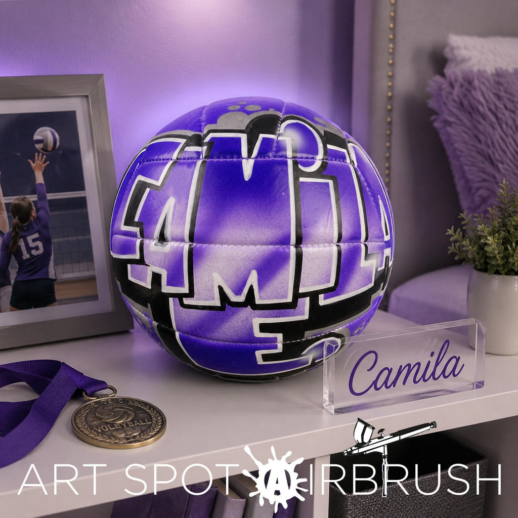 a purple custom volleyball personalized with the name "Camila", placed on a shelf next to a medal and a clear glass display case.
