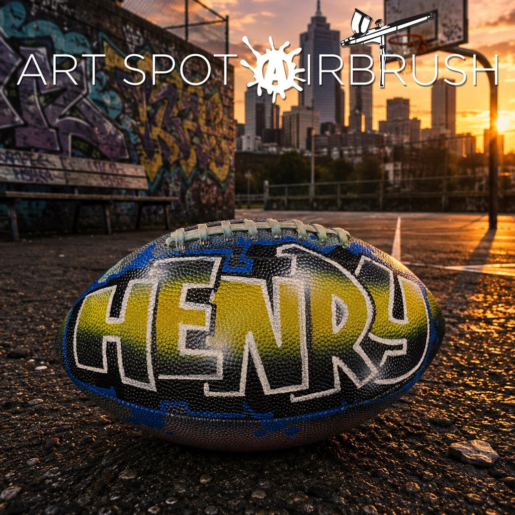 A custom football personalized with the name "HENRY" painted on it, sitting on a basketball court with graffiti in the background and a city skyline visible at sunset.