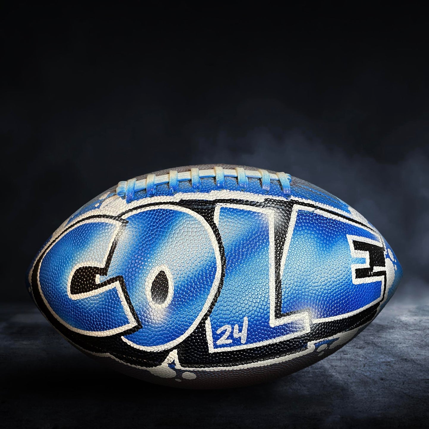 A blue and black football with the name "Cole" written on it, sitting on a dark surface.