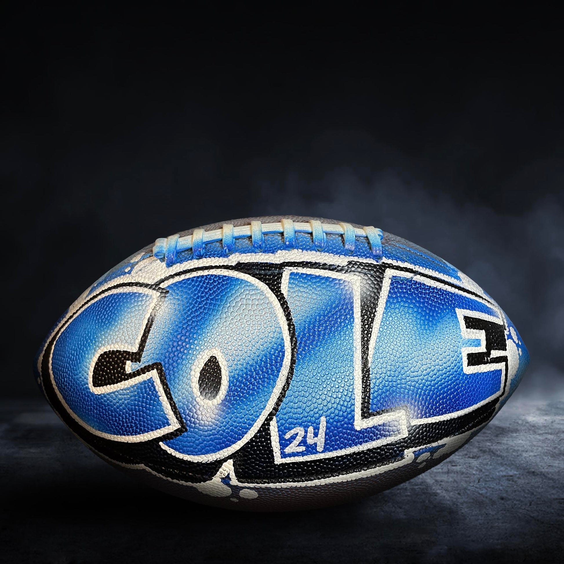 A blue and black football with the name "Cole" written on it, sitting on a dark surface.
