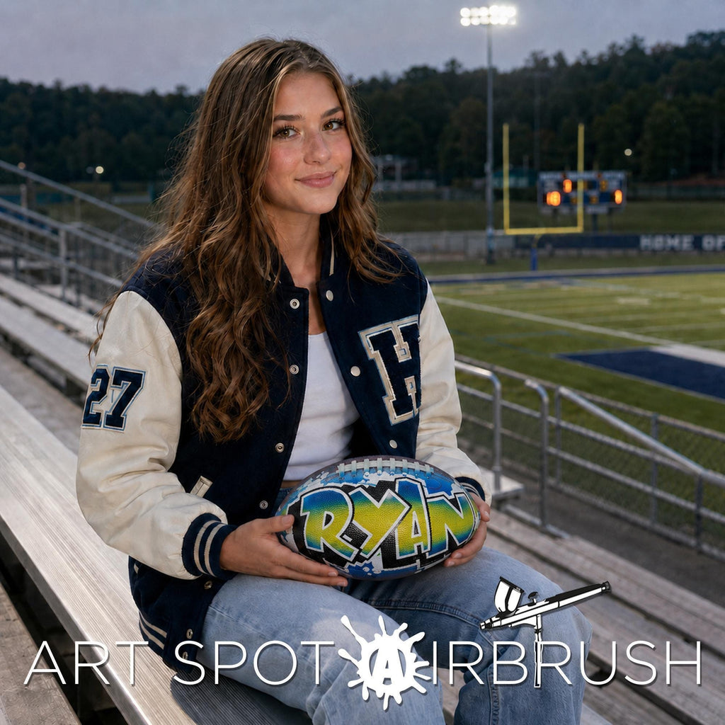 A young woman with long brown hair is sitting on bleachers, holding a custom-painted football with the name "RYAN" on it.