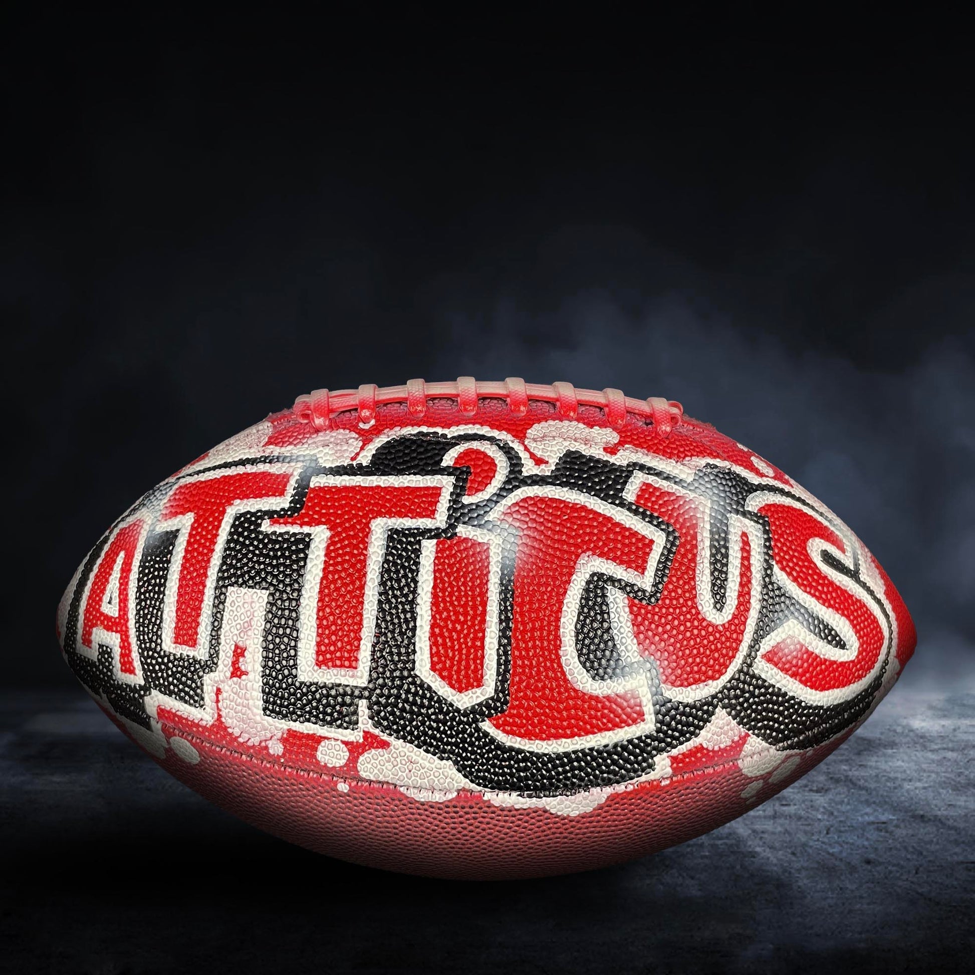 A red and black football with the word "ATLICUS" written on it, against a dark background with smoke.