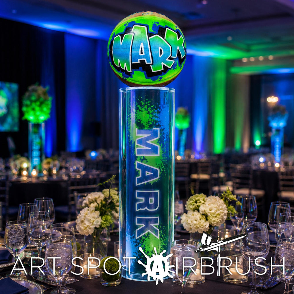A table setting with a large illuminated sign that says "MARK" in a neon green and blue color scheme, surrounded by white flowers and other decorative elements.