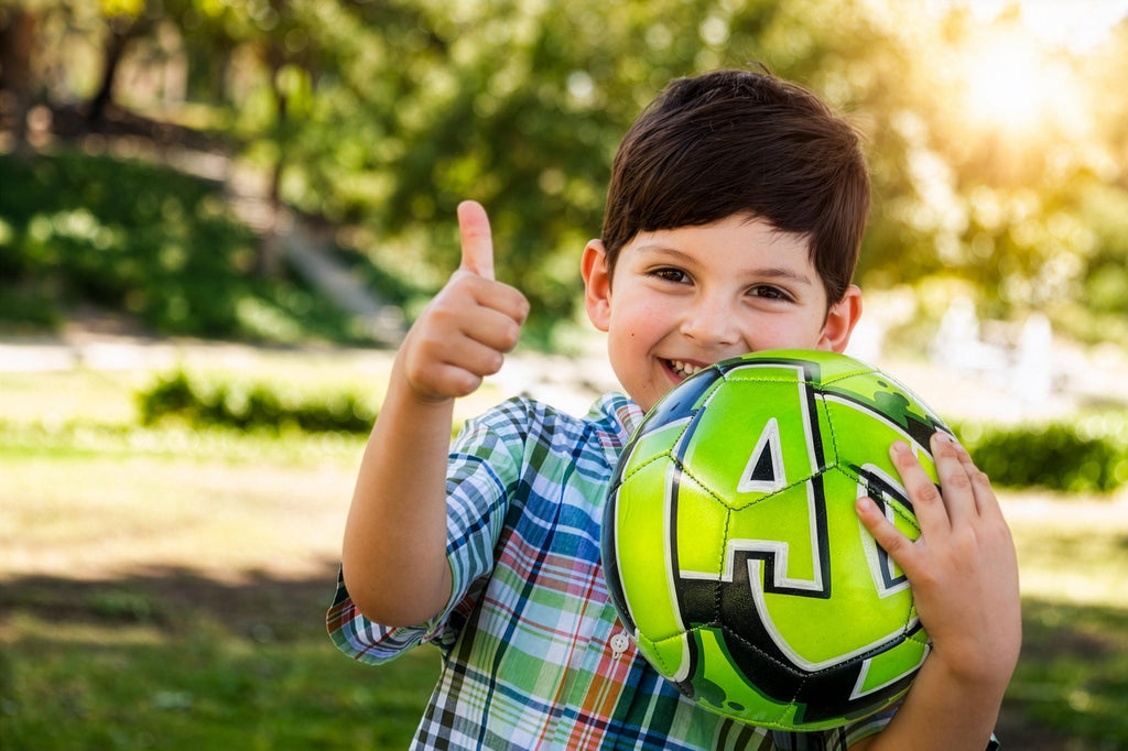 A young boy is smiling and giving a thumbs up while holding a green soccer ball.