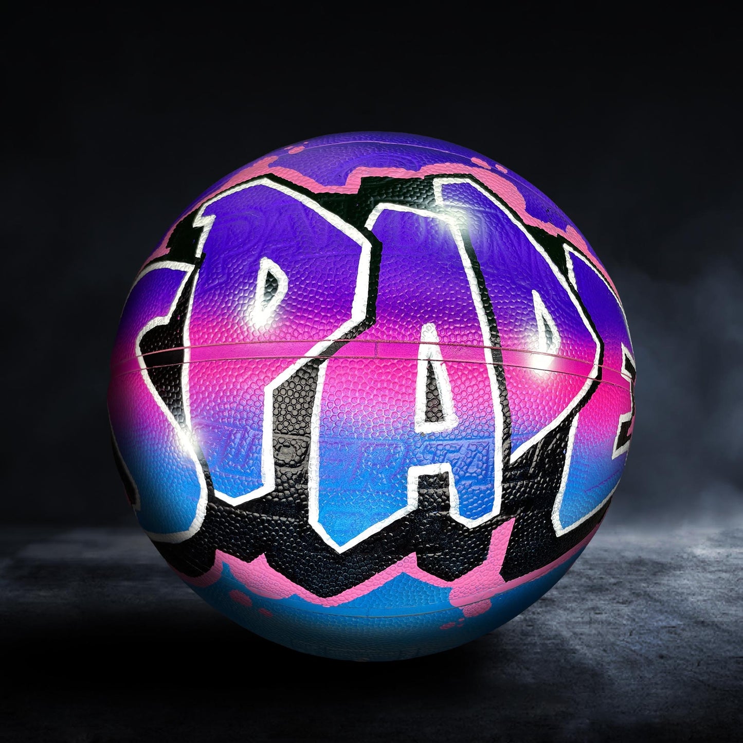 A colorful basketball with the word "PAD" painted on it, set against a dark background.