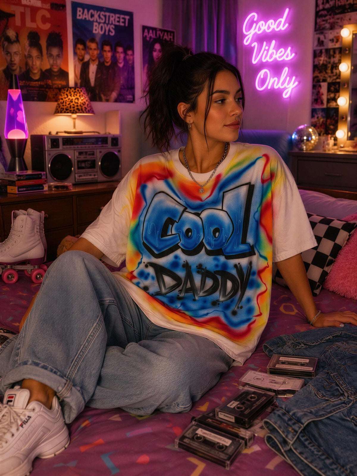 A young woman sitting on a bed, wearing a tie-dye shirt with the text "Cool Daddy" and surrounded by various items, including cassette tapes and a neon sign that says "Good Vibes Only".