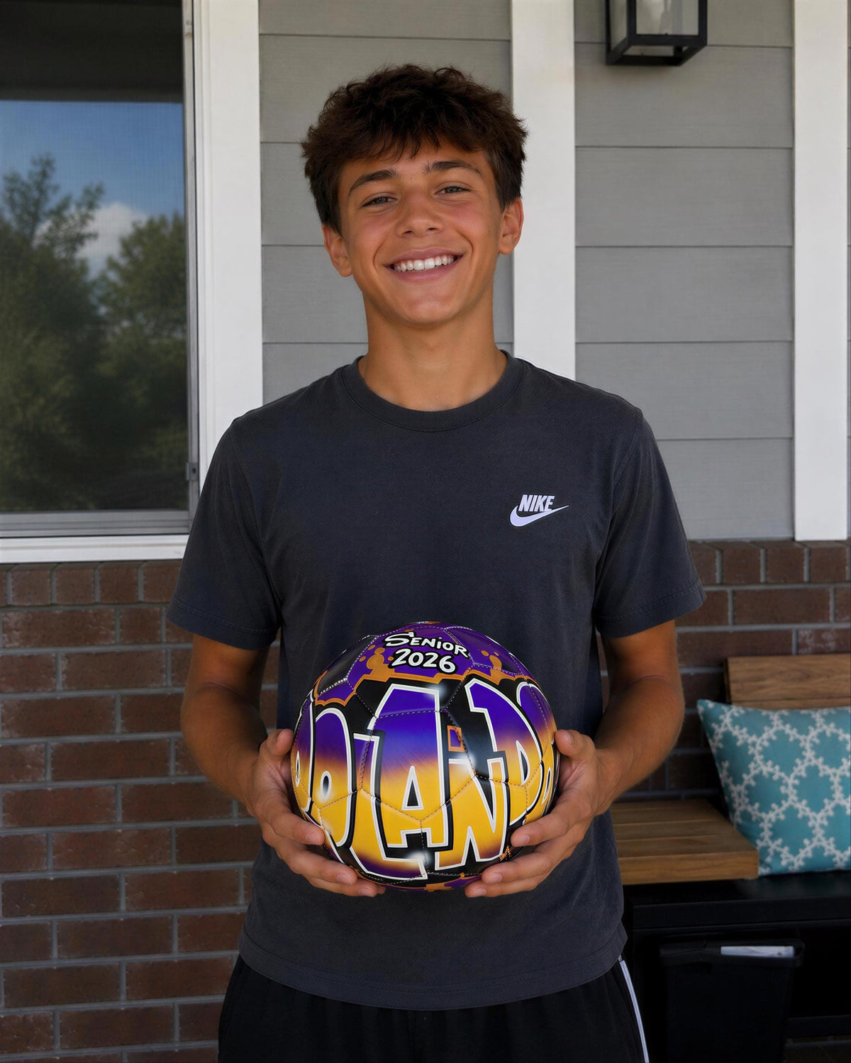 A young man is holding a soccer ball with the word "ORLAND" written on it, smiling at the camera.