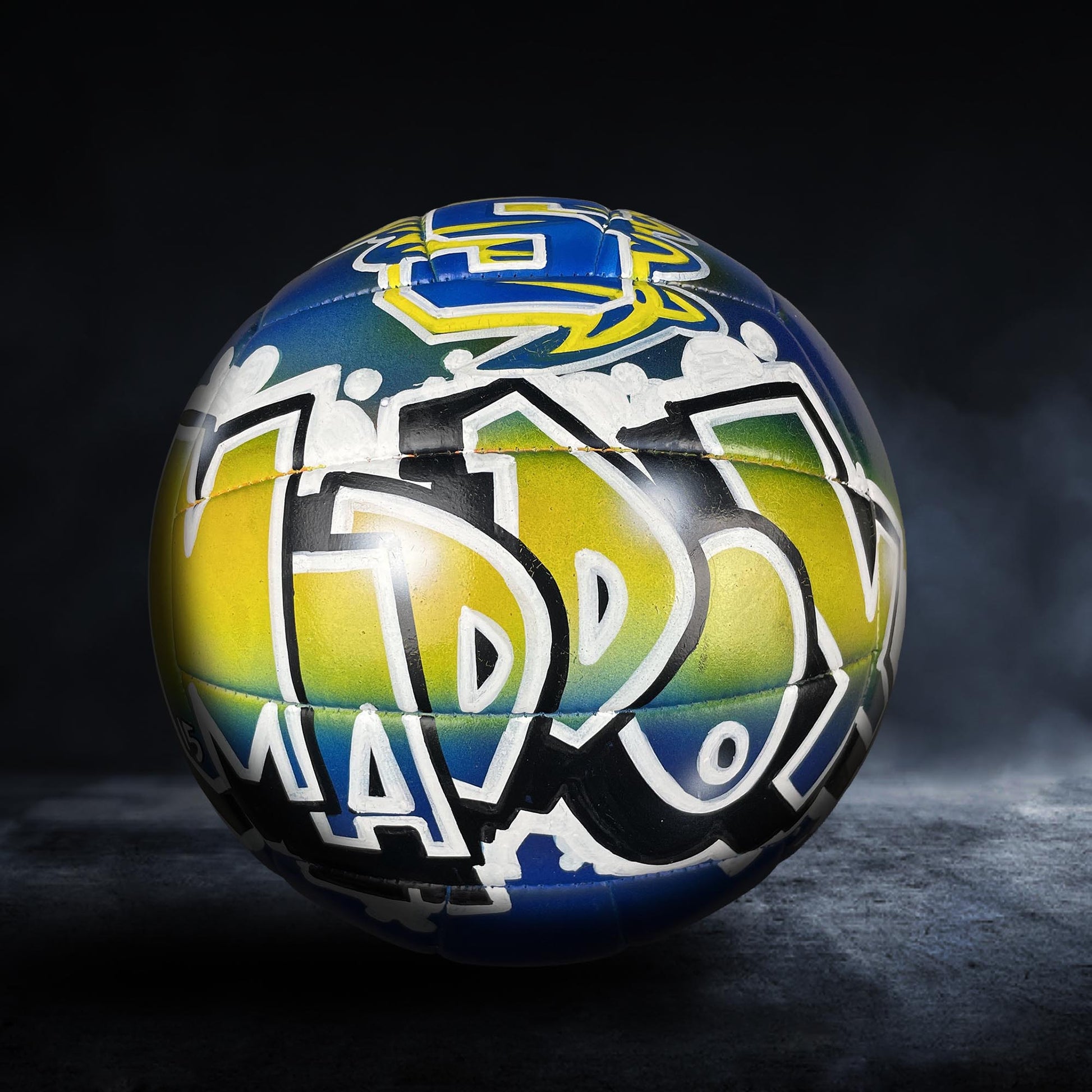 A colorful soccer ball with graffiti-style lettering on it, set against a dark background.