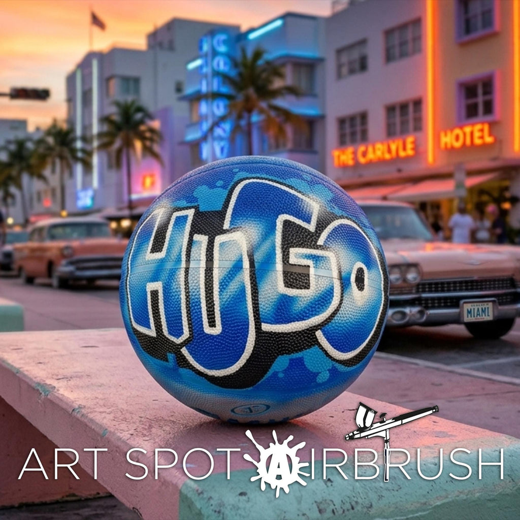 A blue basketball with the word "HUGO" painted on it, sitting on a ledge in front of a brightly lit hotel and palm trees.