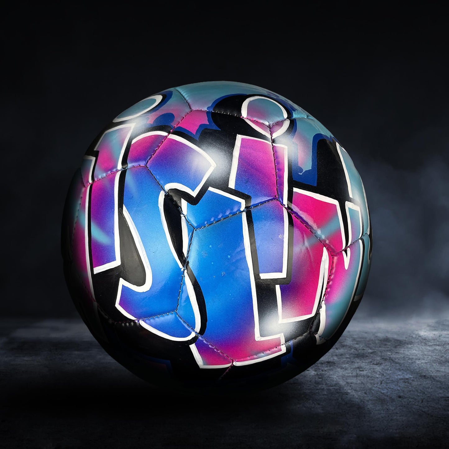 A colorful soccer ball with graffiti-style lettering on it, set against a dark background.