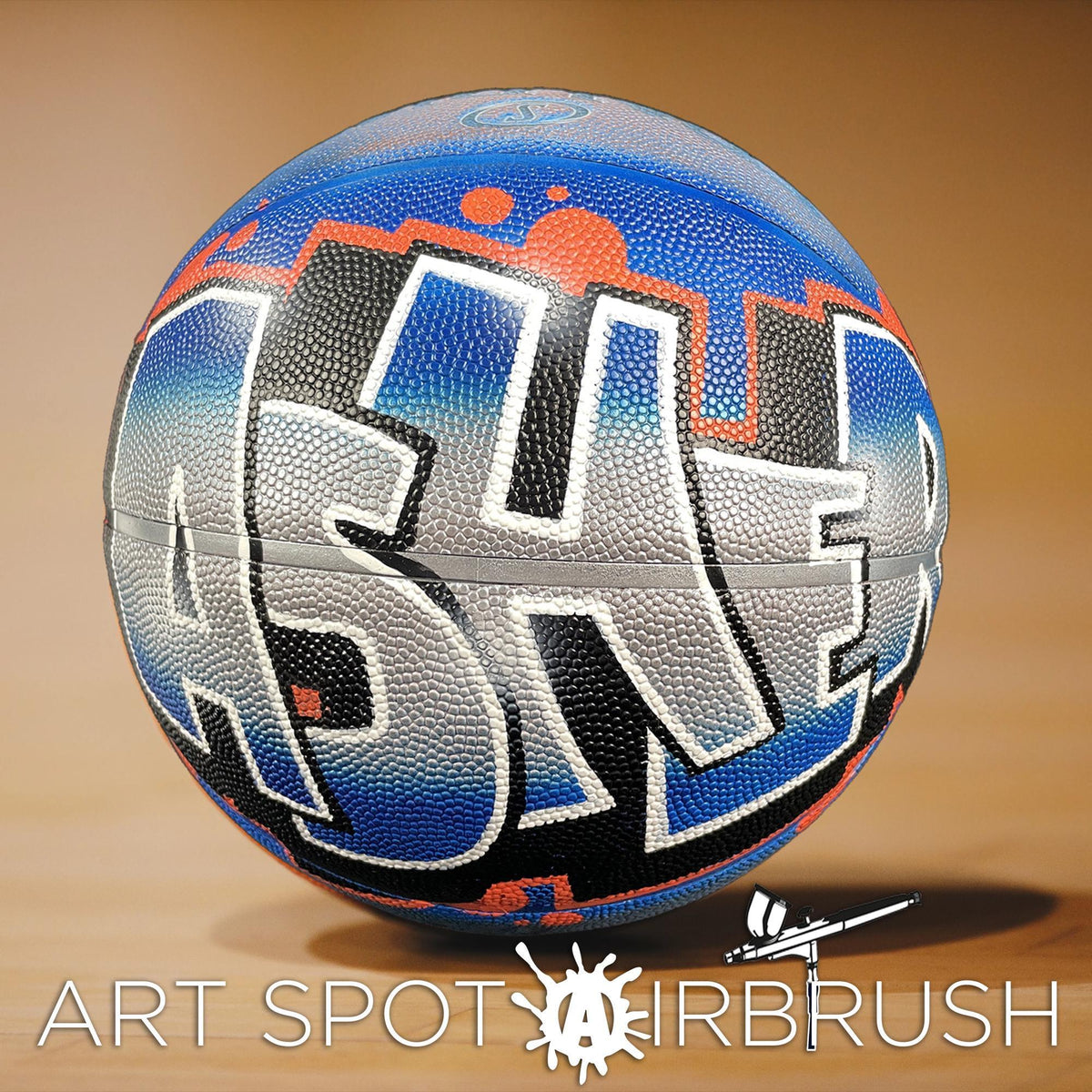 A basketball with graffiti-style lettering on it, sitting on a wooden surface.