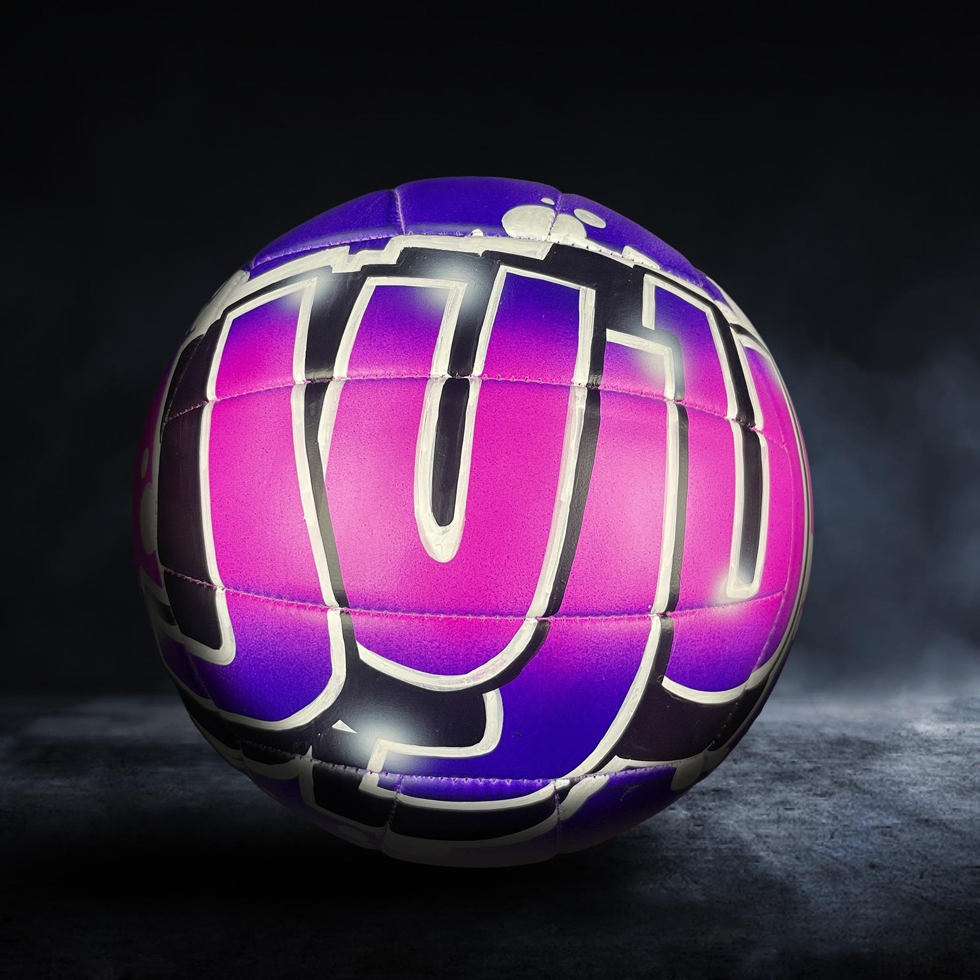 A purple and black sports ball with the word "JU" written on it, against a dark background.
