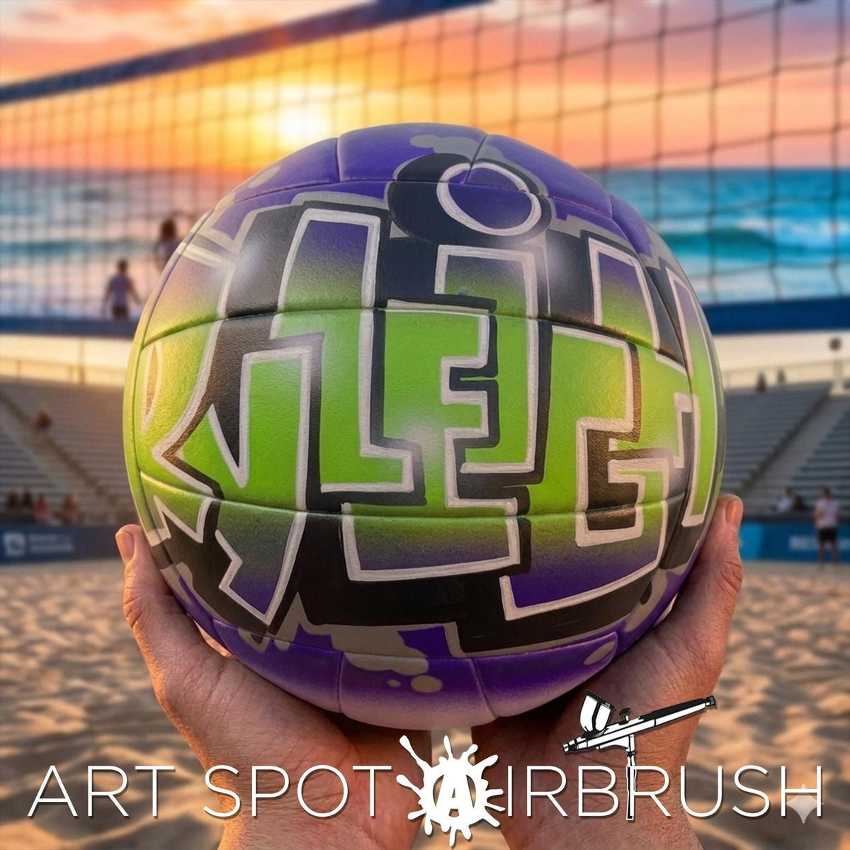 A hand holding a colorful custom volleyball personalized with graffiti-style lettering on it, with a beach volleyball net and sunset in the background.