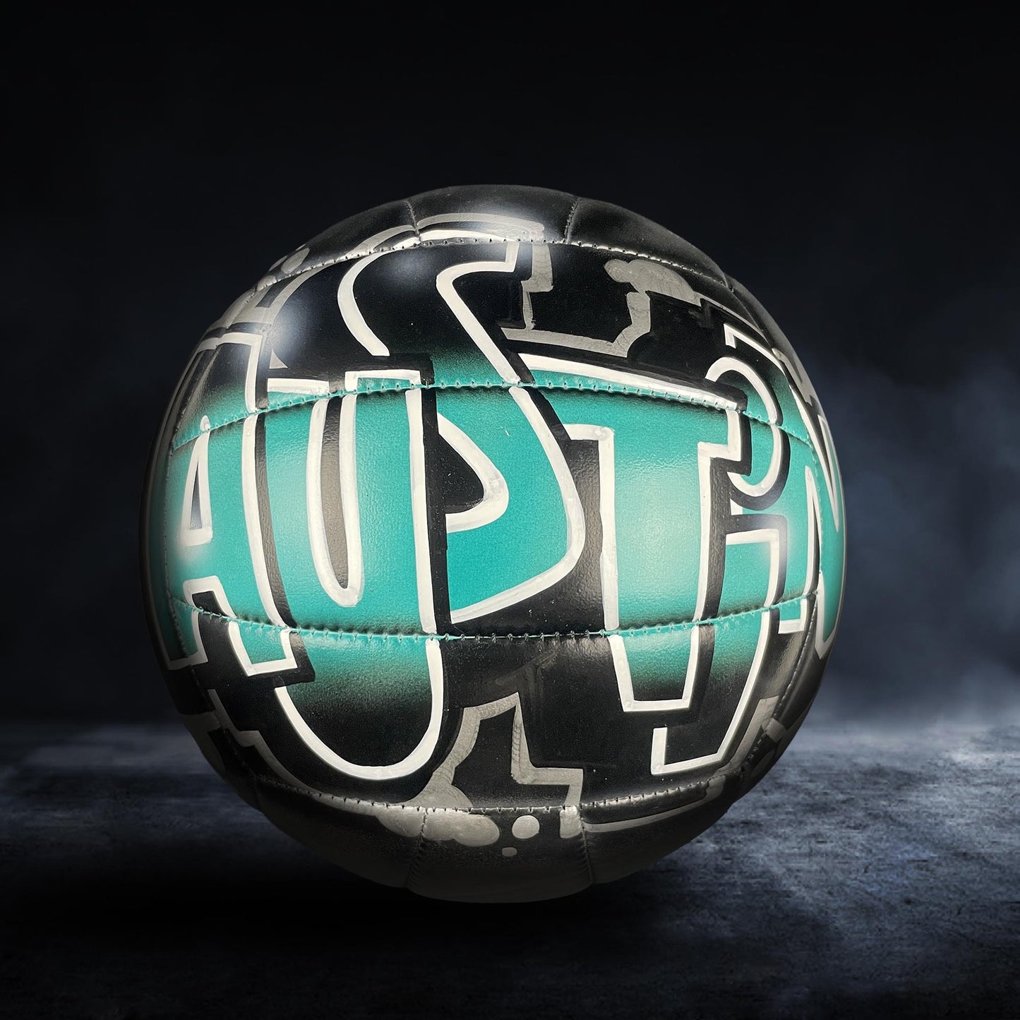 A soccer ball with the word "AUSTIN" painted on it, set against a dark background with a misty or foggy effect.