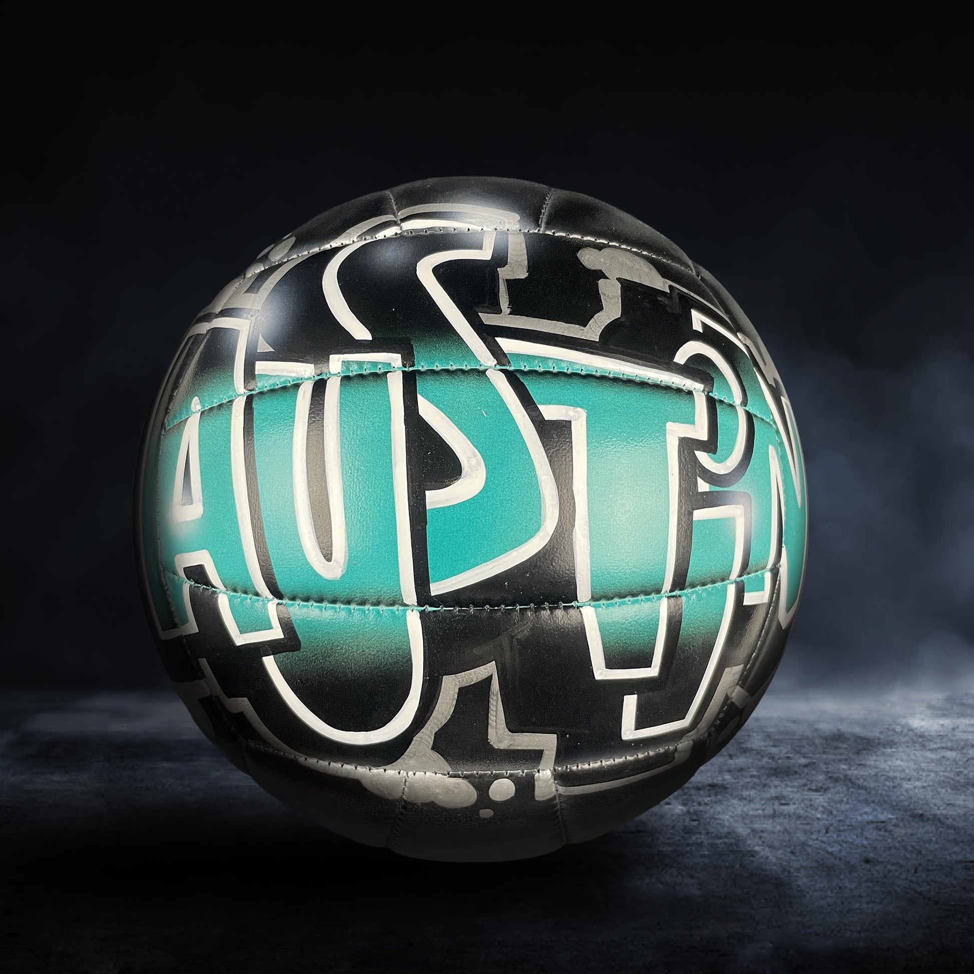 A soccer ball with the word "AUSTIN" painted on it, set against a dark background with a misty or foggy effect.