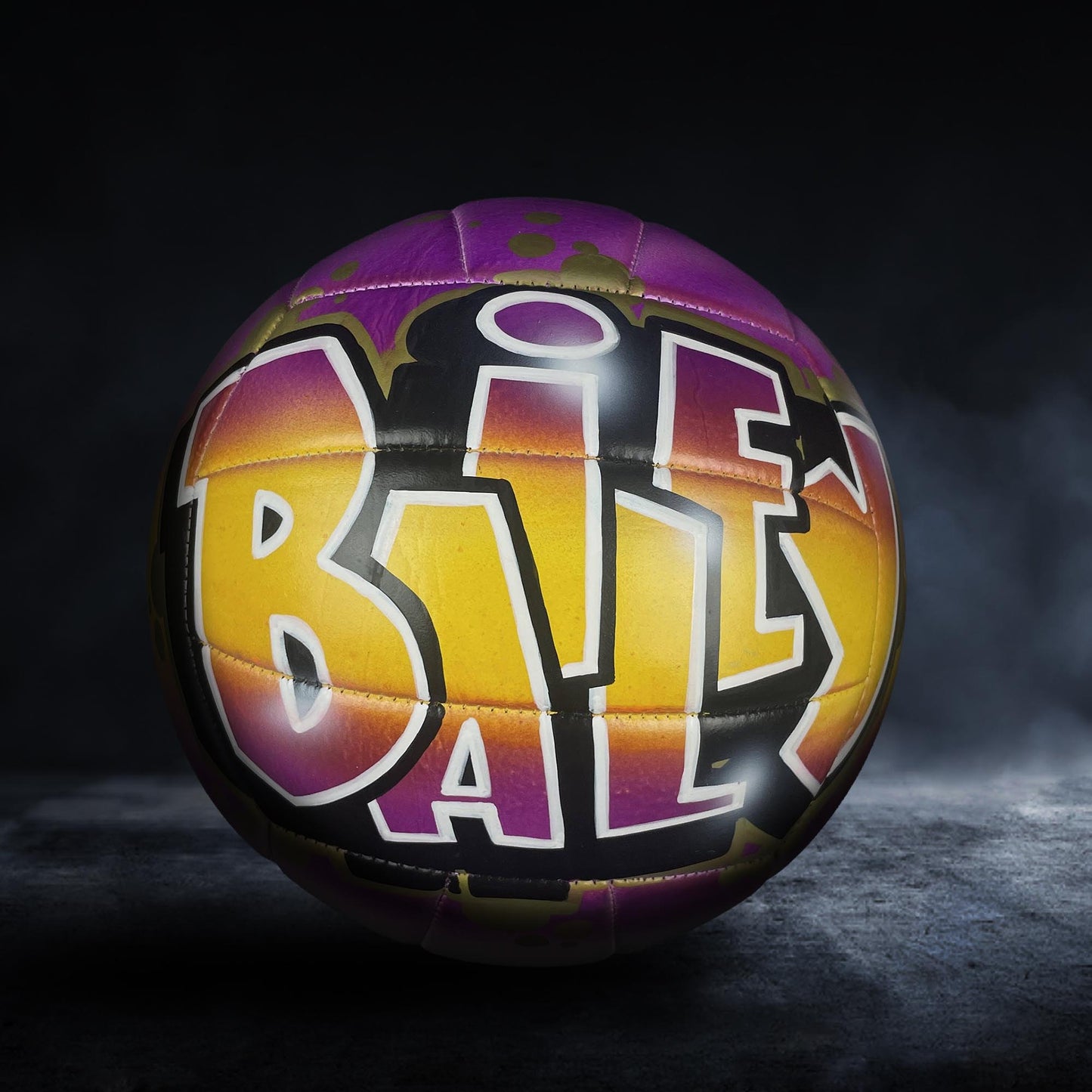 A colorful volleyball with the word "BAL" painted on it, set against a dark background with a misty or foggy effect.