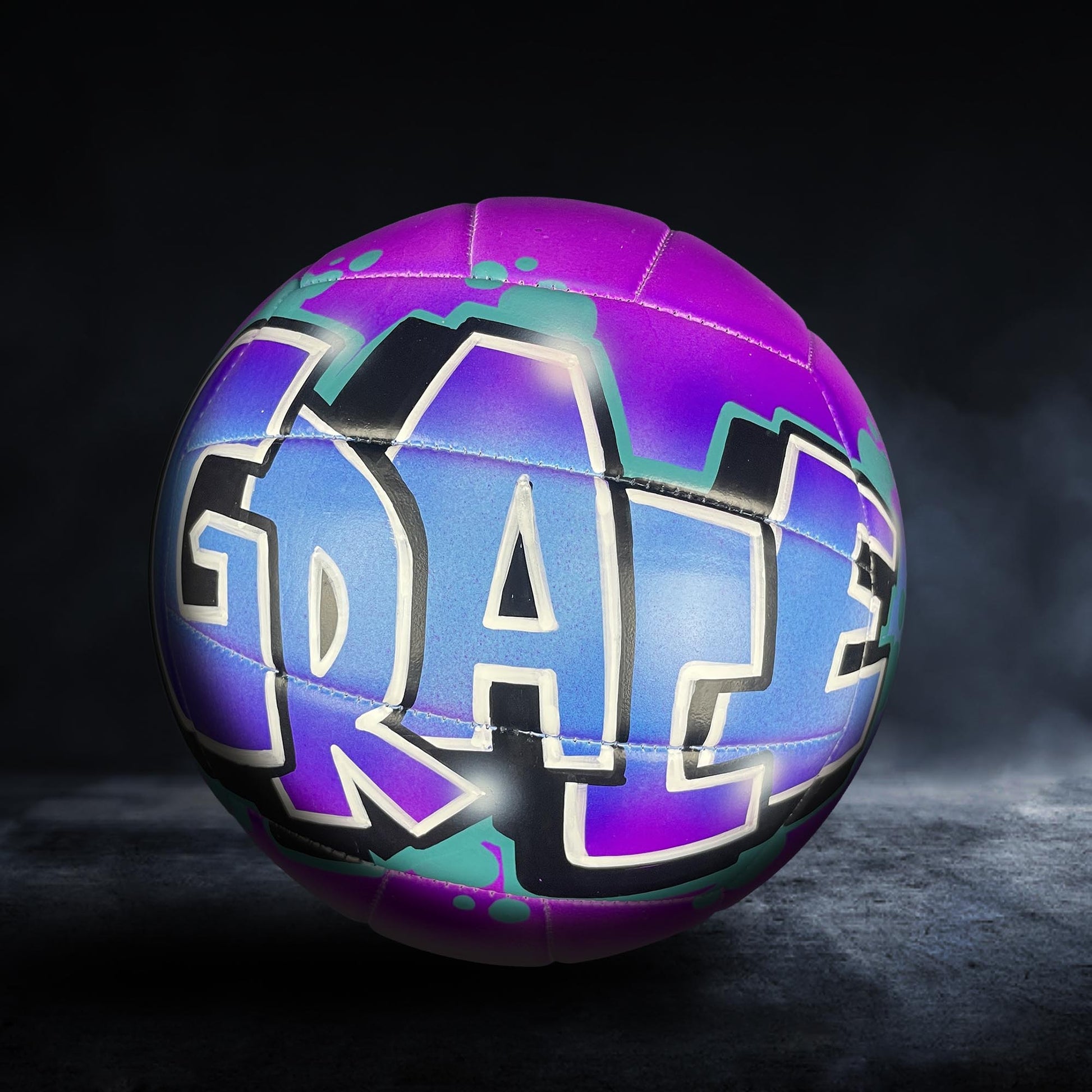 A colorful volleyball with the word "Dazzle" painted on it, set against a dark background.
