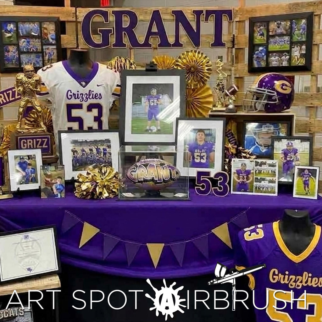 The image is a display featuring a collection of framed photos, jerseys, and memorabilia related to the Grizzly football team, including images of players and coaches, and a custom football personalized with the name Grant..