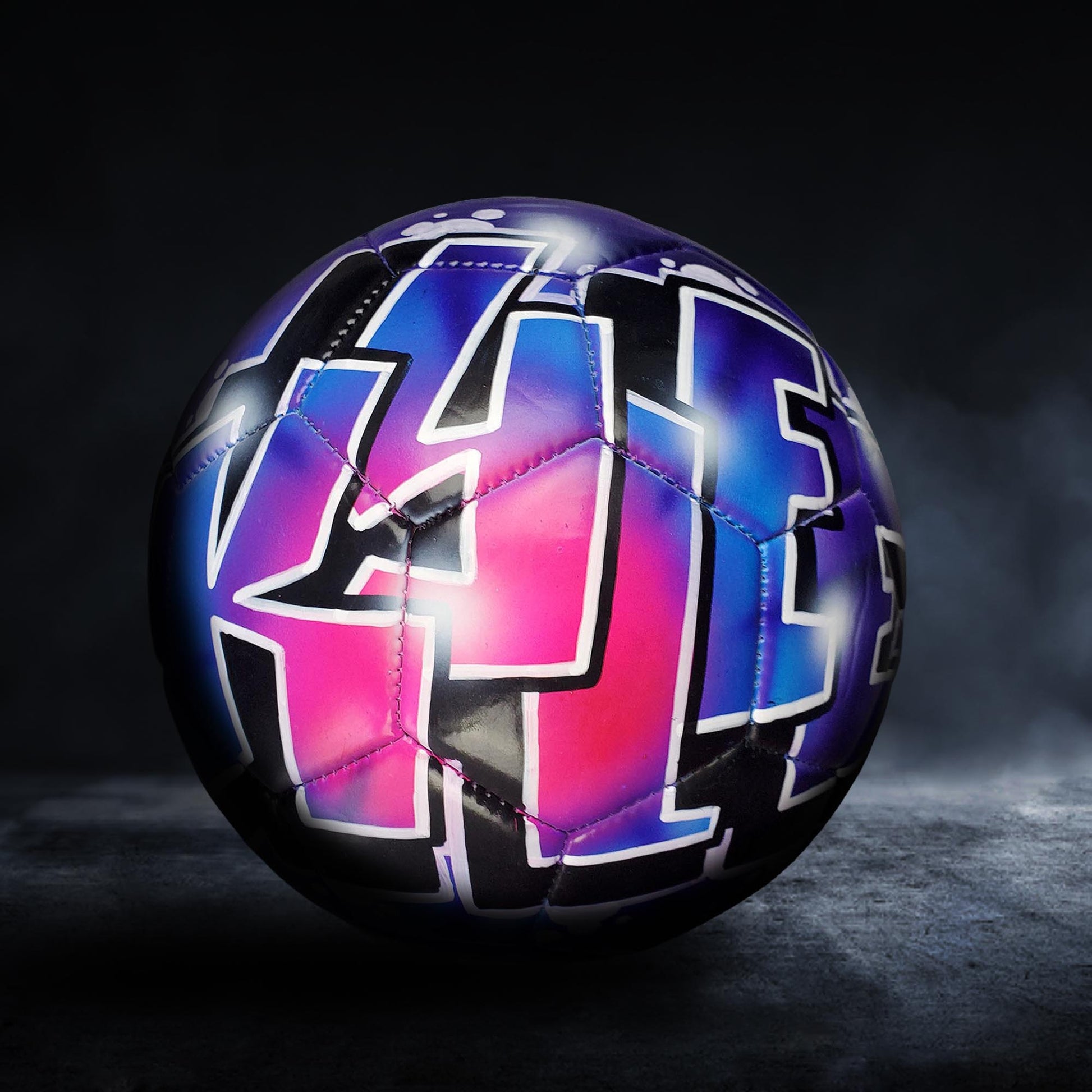 A colorful soccer ball with graffiti-style lettering on it, set against a dark background.
