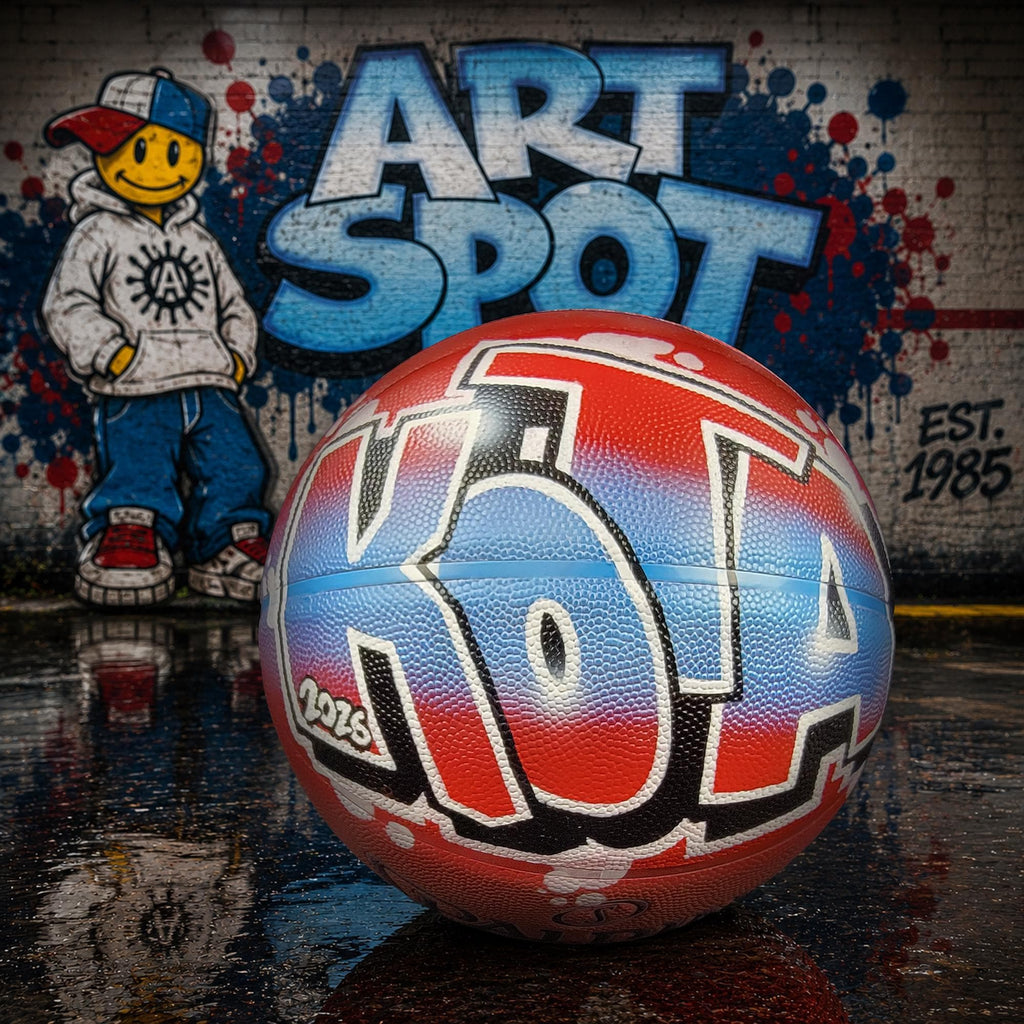 A basketball with colorful graffiti on it, placed on a wet surface, with a graffiti-covered wall in the background.