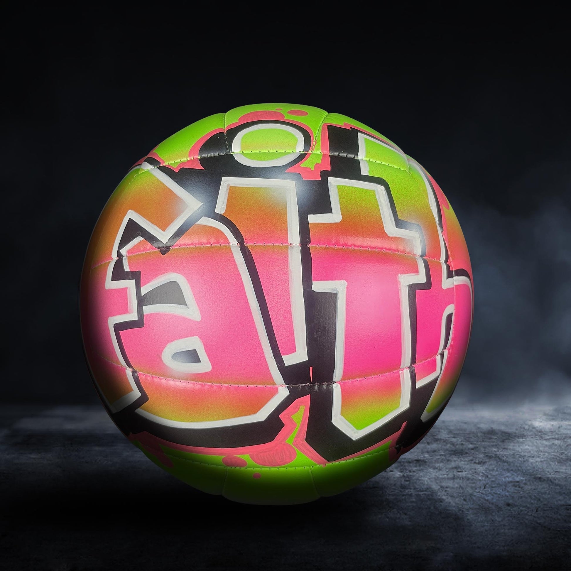 A colorful, graffiti-style soccer ball with the word "Faith" painted on it, set against a dark background.