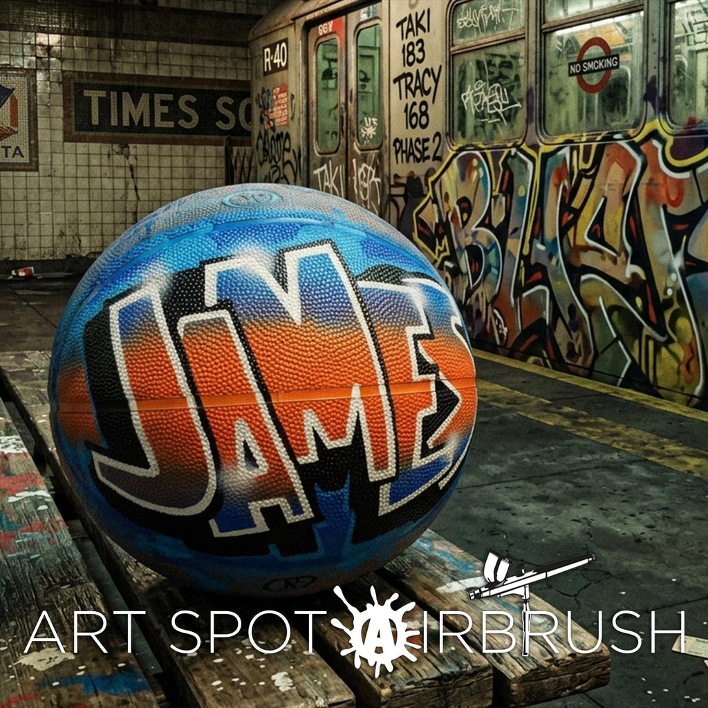 A large, colorful basketball with the name "JAMES" painted on it, sitting on a wooden bench in an urban setting with graffiti on the walls in the background.
