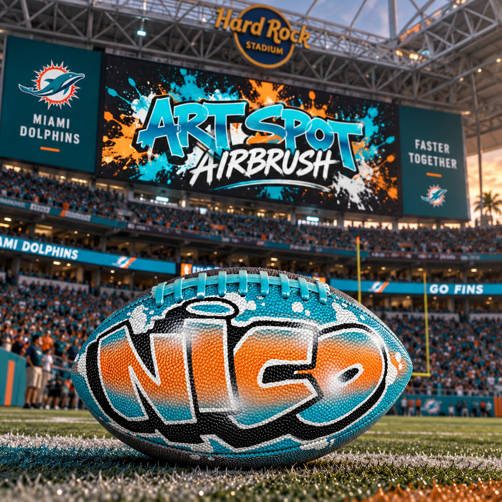 a football with the word "Nico" painted on it, placed on a football field in front of a stadium.