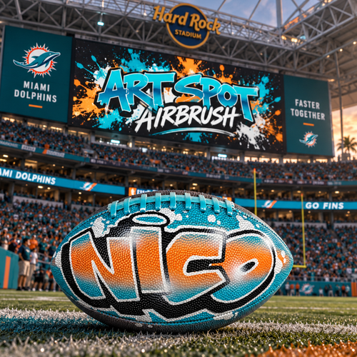a football with the word "Nico" painted on it, placed on a football field in front of a stadium.