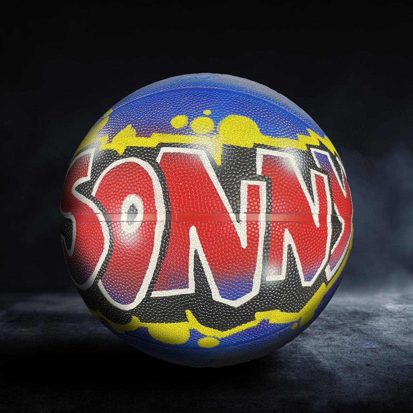 A colorful basketball with graffiti-style text on it, placed on a dark surface.