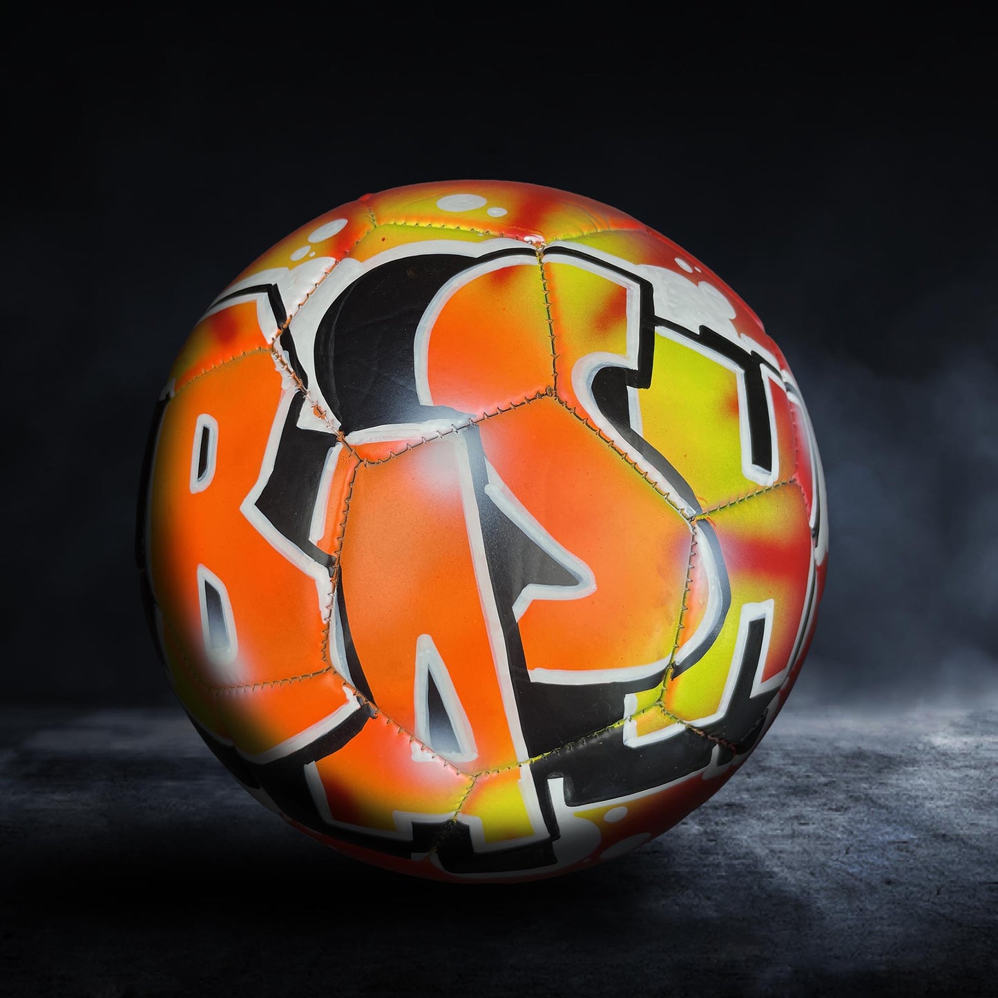 A colorful soccer ball with graffiti-style lettering on it, set against a dark background.