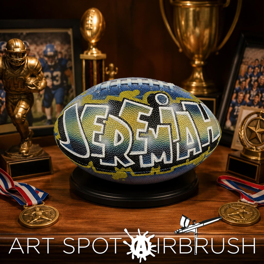 a personalized custom football with the name "JEREMIAH" painted on it, surrounded by various sports memorabilia such as trophies, medals, and a football helmet.