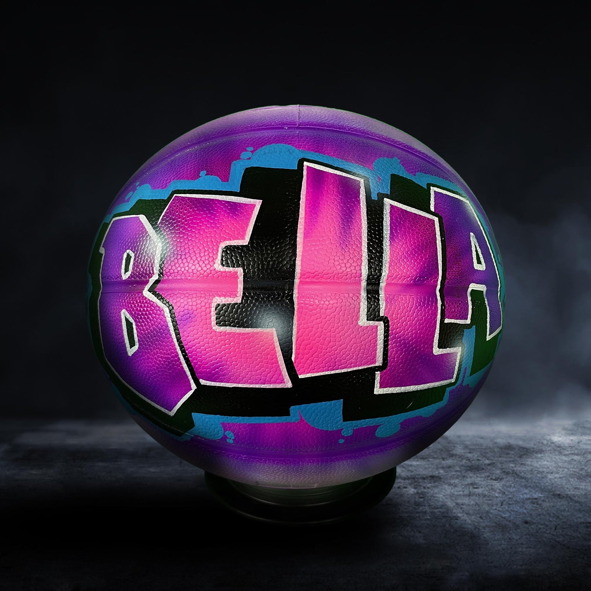 A basketball with the name "Bella" painted on it in a colorful, graffiti-style design.