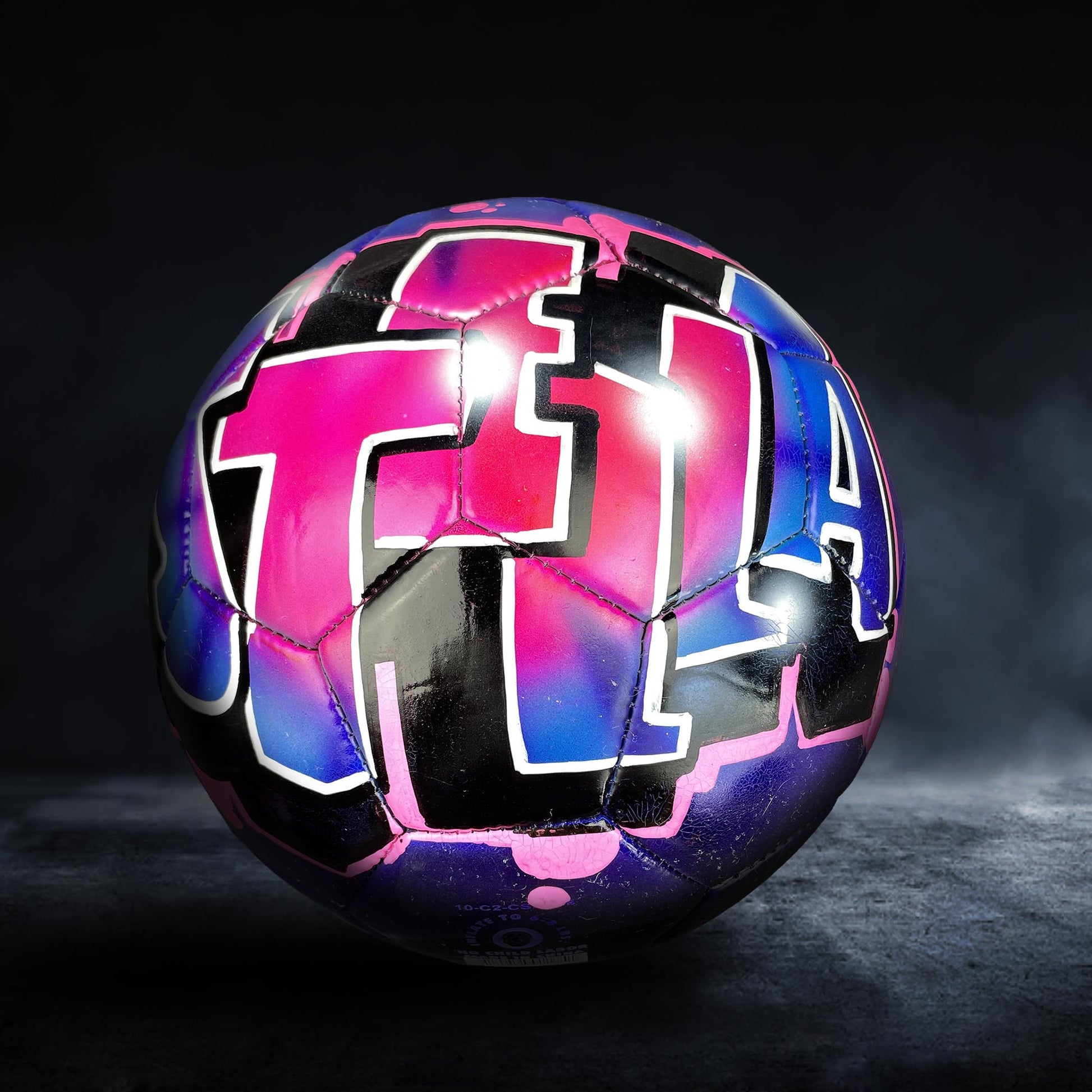 A colorful soccer ball with graffiti-style lettering on it, set against a dark background.